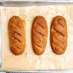 three loaves of bread sitting on top of a baking sheet with parchment paper next to them