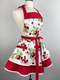 an apron dress with cherries on it and a red sash around the waist is worn by a mannequin