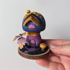 a hand holding a tiny purple and yellow house