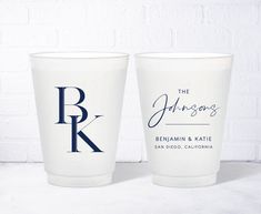 two white cups with blue lettering on them sitting next to each other in front of a brick wall