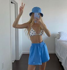 a woman taking a selfie while wearing a blue hat and shorts in her bedroom