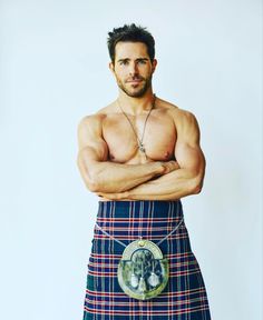 a man in a kilt with his arms crossed, posing for a photo against a white background