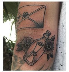 a tattoo on the arm of a person with an envelope and flowers in it's bottle