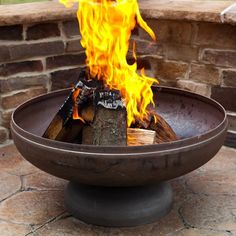 a fire pit sitting on top of a stone floor next to a brick wall with flames coming out of it