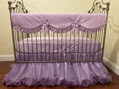 a baby crib with purple ruffled bedding on the bottom and side rails