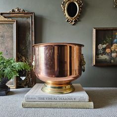 a large metal pot sitting on top of a book next to two framed pictures and a plant