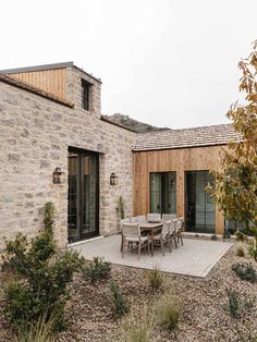 an outdoor patio with table and chairs next to a stone building that is made out of wood