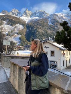 a woman is sitting on a ledge looking at the snow covered mountains in the background