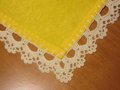 a piece of yellow cloth with white lace on it sitting on top of a wooden table