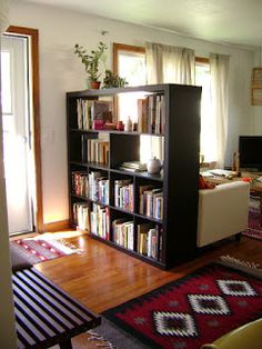 a living room filled with furniture and bookshelves next to a window on top of a hard wood floor