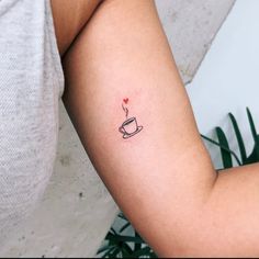 a woman's arm with a small coffee cup tattoo on it