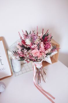 a bouquet of flowers sitting on top of a white table next to a book and yarn