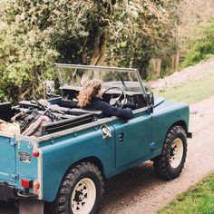 a woman is sitting in the back of a blue jeep with her hood up and looking out