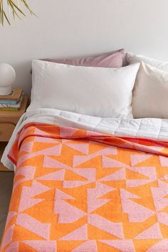 a bed with an orange and pink blanket on top of it next to a plant