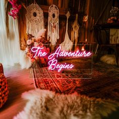 a neon sign that says the adventure begins in front of some chairs and rugs