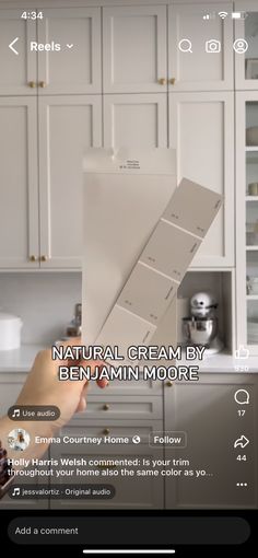 a person holding up some white paint in a kitchen with the words natural cream by benjamin moore on it