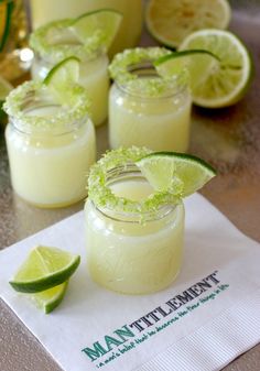 three margaritas with lime garnish sit on a napkin next to two glasses