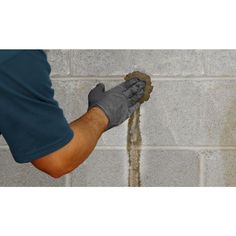 a person wearing gloves and holding a sponge in front of a brick wall that has been stripped off