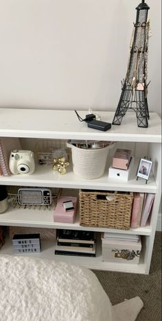 a white shelf with baskets, books and other items on it in front of the eiffel tower