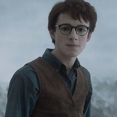 a young man with glasses standing in front of a snow covered mountain and looking at the camera