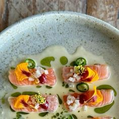 a white plate topped with salmon and cucumber on top of green leafy sauce