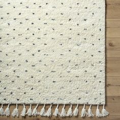 a white rug with black dots and tassels on the bottom is laying on a wooden floor