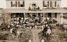 a group of people standing in front of a house with two horses and one donkey