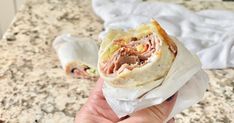 a hand holding a wrap filled with meat and veggies on top of a counter