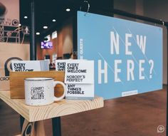 two coffee mugs sitting on a table in front of a sign that says, new here?