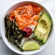 a bowl filled with rice, salmon and avocado on top of a table