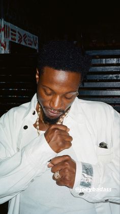 a man in a white shirt is tying his gold chain around his neck and looking down at his watch