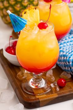 two glasses filled with drinks sitting on top of a wooden tray next to pineapples