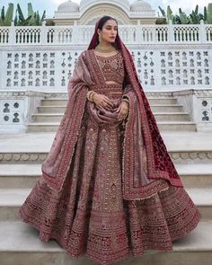 a woman standing on some steps wearing a red and gold bridal gown with matching dupatta