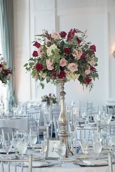 a tall silver vase filled with lots of flowers on top of a table covered in white linens