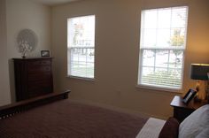 a bedroom with two windows and a dresser in it's corner, next to a bed