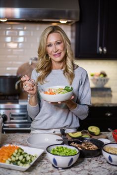 a woman holding a bowl of food in her hands while standing at the kitchen counter