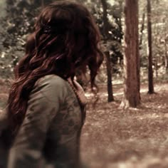 a woman with long hair walking through the woods