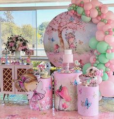 a table topped with lots of pink and green balloons next to a giant balloon arch