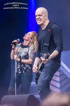 two people on stage with microphones in front of them and one person holding an electric guitar