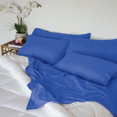 a bed with blue sheets and pillows on top of it next to a plant in a vase