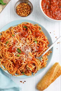 a plate of spaghetti with tomato sauce and parmesan cheese on the side next to breadsticks