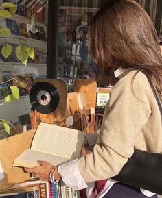 a woman reading a book in front of a store window with lots of books on display