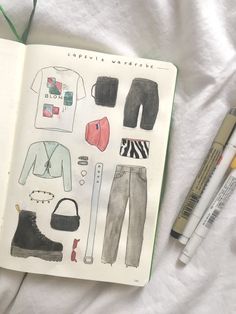 an open notebook with clothes and accessories on it next to markers, pencils and marker pens