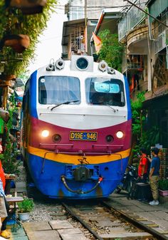 a colorful train traveling down tracks next to people