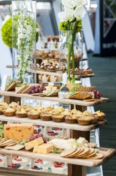 an assortment of food is displayed on wooden trays at a buffet table with flowers in vases