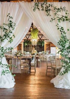 an indoor wedding venue with white drapes and greenery on the ceiling, along with wooden flooring