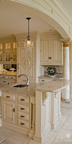 a large kitchen with marble counter tops and white cabinets, along with an archway leading to the dining room