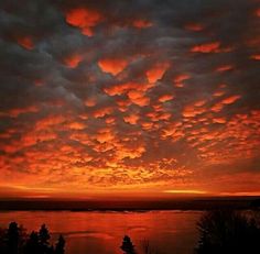 the sky is filled with red clouds as the sun sets in the distance over water