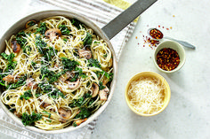 a pan filled with pasta, mushrooms and spinach next to two bowls of seasoning