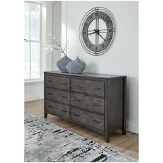 a large clock mounted to the side of a wall next to a dresser with drawers